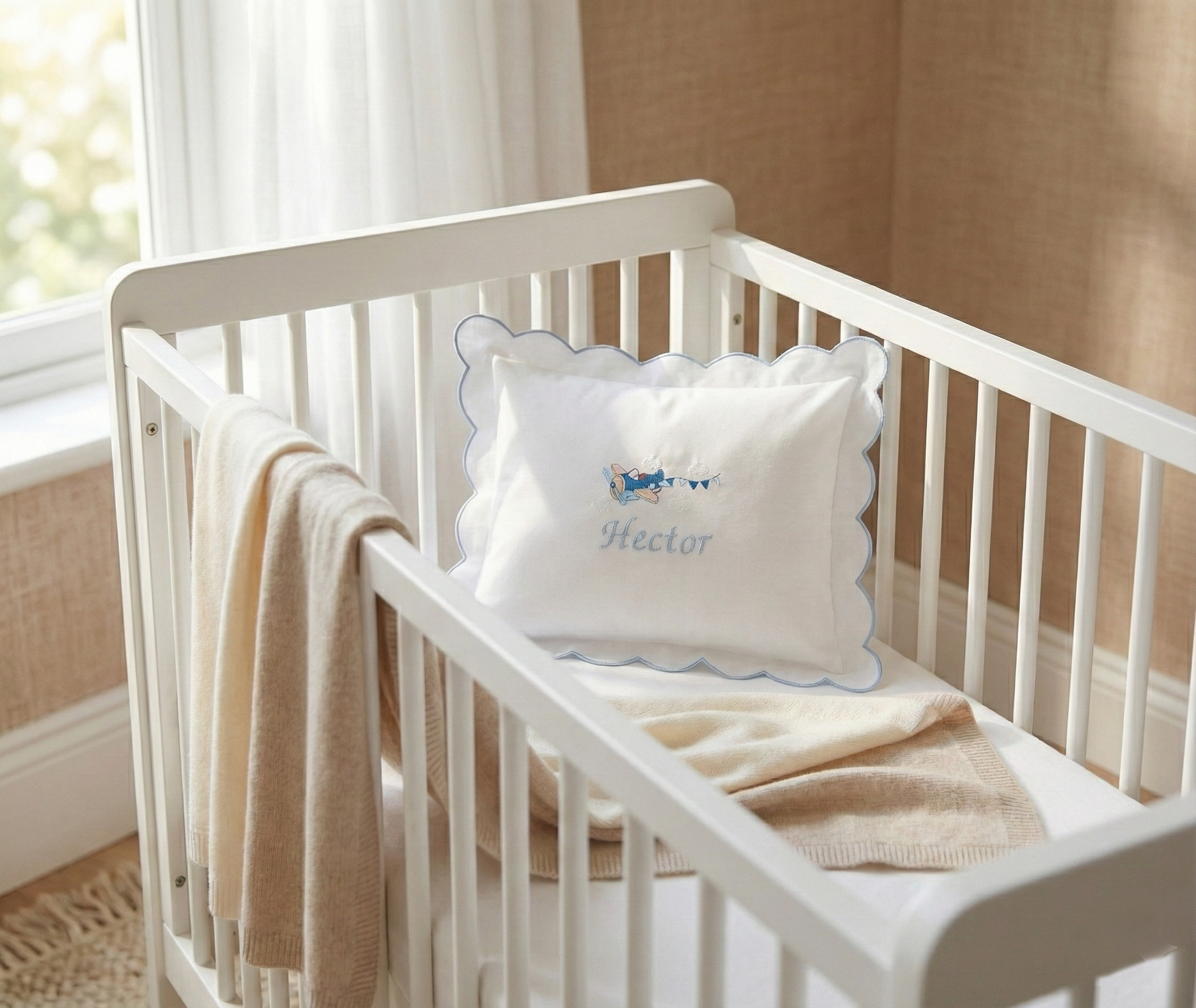 White crib with a decorative pillow and blanket in a nursery setting. Personalised baby pillowcase with embroidered name in soft cotton, luxury newborn keepsake gift UK