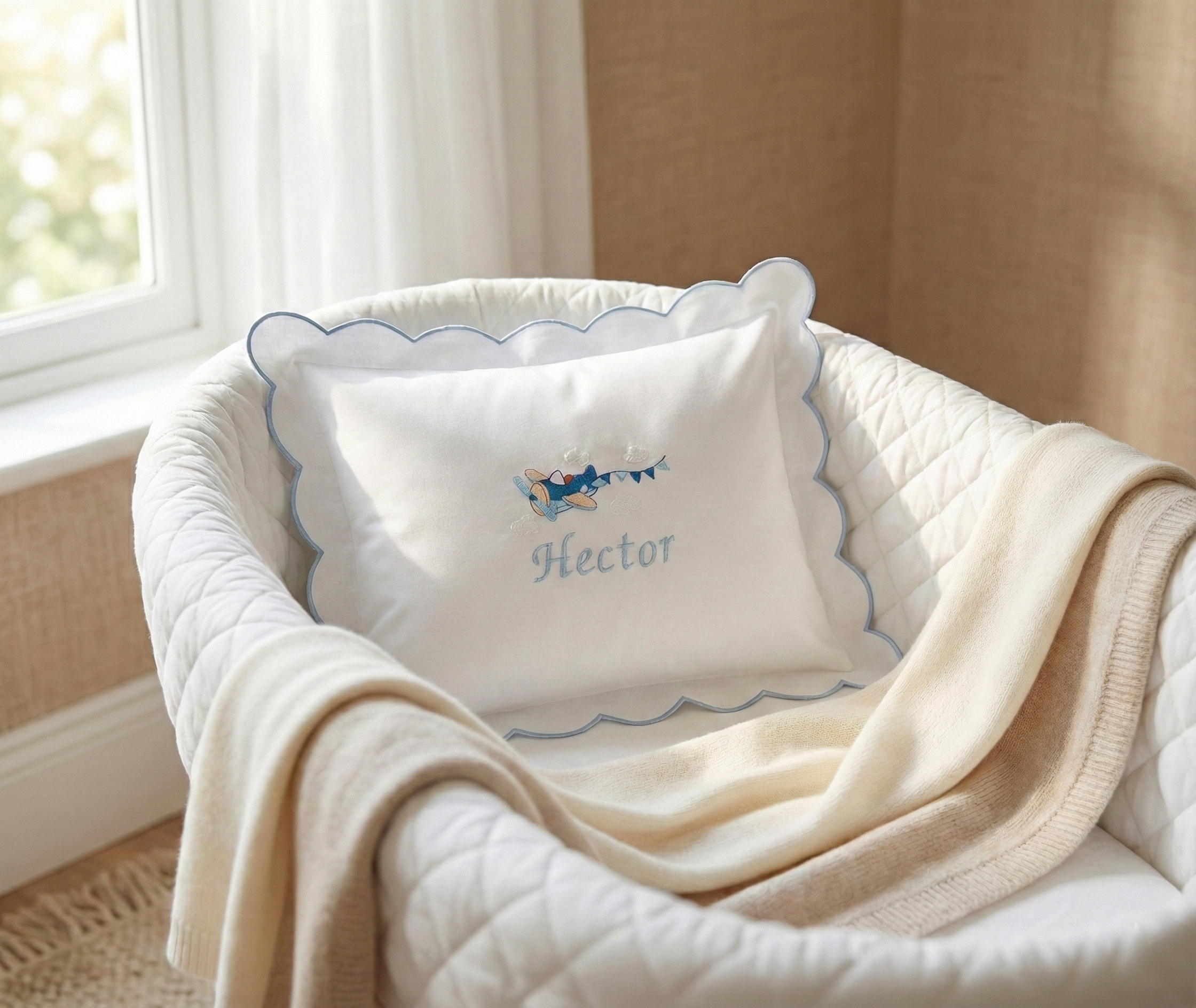 Baby crib with white crib sheet, beige blanket, and decorative pillow with 'Hector' embroidery. Personalised baby pillowcase with embroidered name in soft cotton, luxury newborn keepsake gift UK