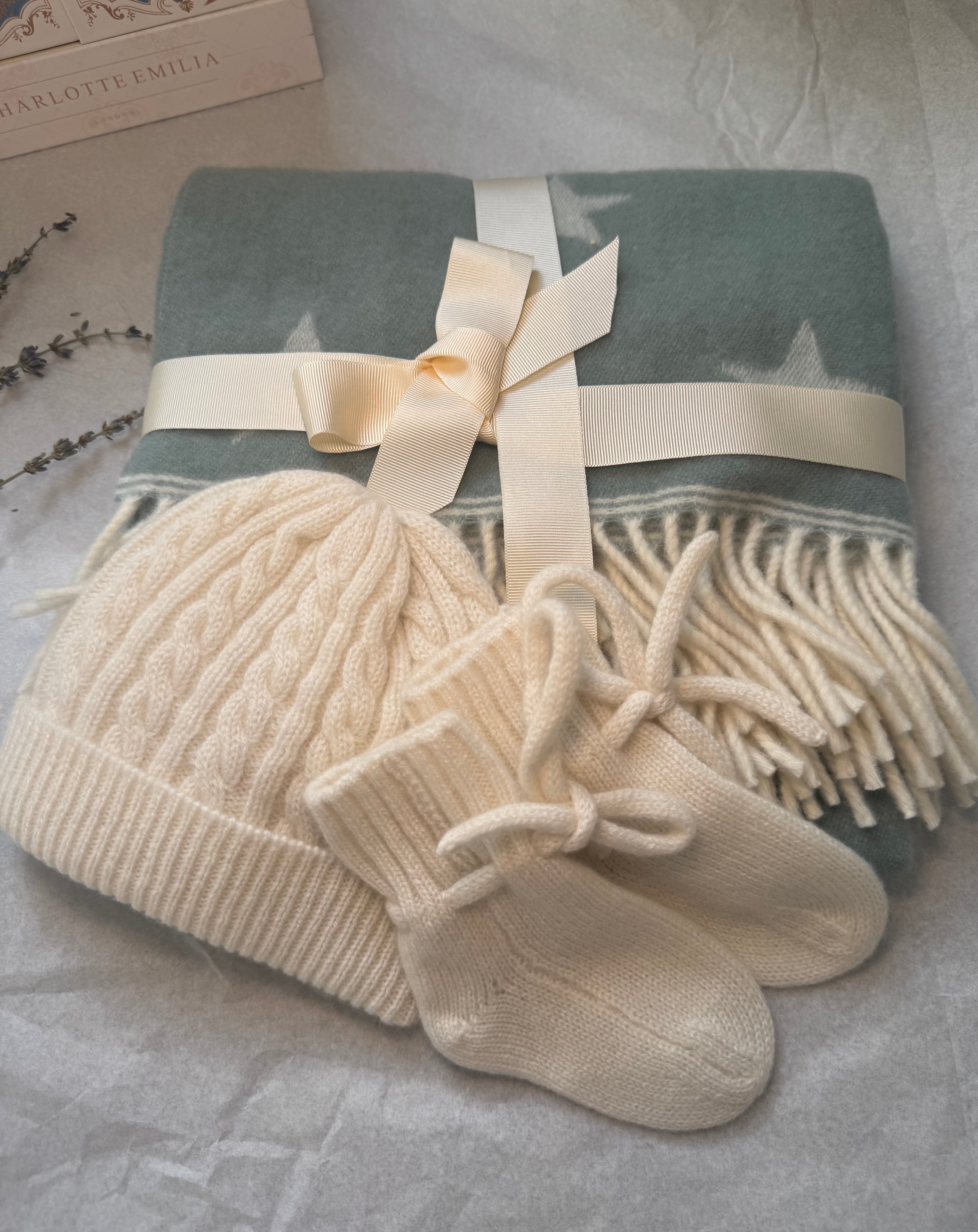 Set of baby hat, mittens, and blanket with a bow on a textured surface