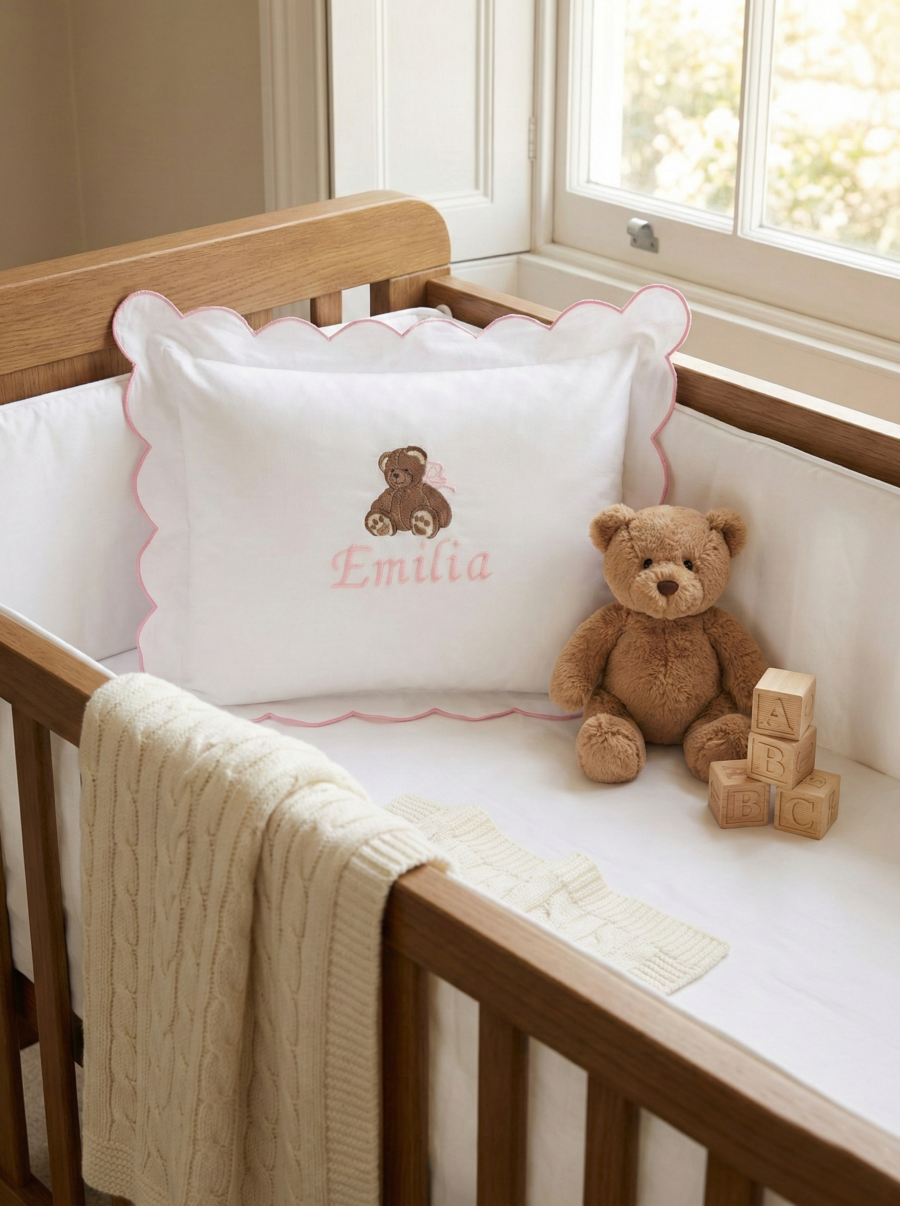 Nursery crib with a teddy bear, blocks, and a personalized pillow. Personalised baby pillowcase styled in neutral nursery, embroidered name cushion luxury baby gift idea